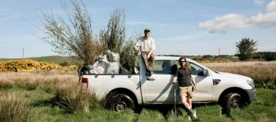 Two people standing by a truck full of tree saplings